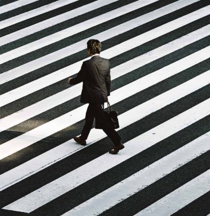 Man in black suit walking across street with white road markings